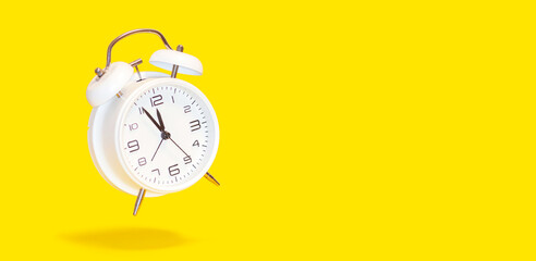 White bell alarm clock hovering over yellow background. 5 to 12 clock concept isolated. 