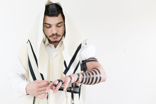 Young Orthodox Jew in shawl (tallit) putting on phylacteries (tefilin) on left arm.