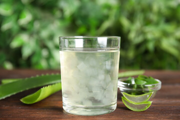 Fresh aloe drink in glass and leaves on wooden table