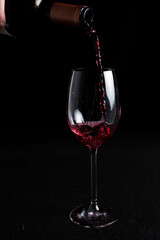 Bottle pouring red wine on a wine glass on a black background with negative space.