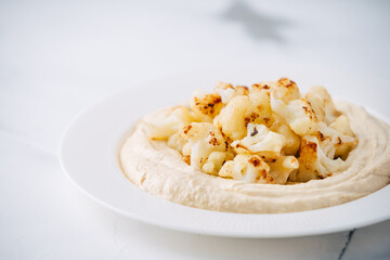 Hummus with fried cauliflower on light concrete background