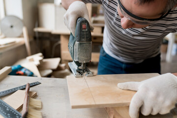 Carpenter working on wood with electric jigsaw in workshop. Joinery work on the production and renovation of wooden furniture. Small Business Concept