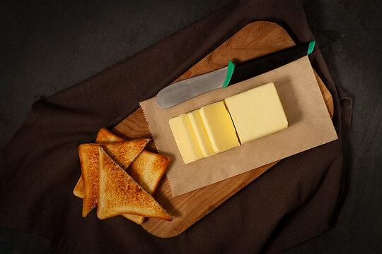 A piece of butter, sliced, on a cutting board, with toast bread, on a black background, no people, horizontal,top view,