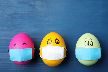 Bright  eggs in protective masks on blue wooden table, flat lay with space for text. Easter holiday...
