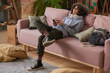 Boy sitting on sofa and playing video game alone in the living room