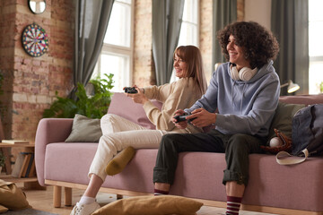Obraz premium Young happy couple sitting on sofa and having fun playing computer video game in the living room