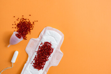 Reusable menstrual cup, sanitary pad and tampon with red glitter on orange background with copy space