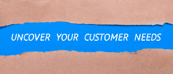 A strip of blue paper with the words UNCOVER YOUR CUSTOMER NEEDS between the brown paper. View from above