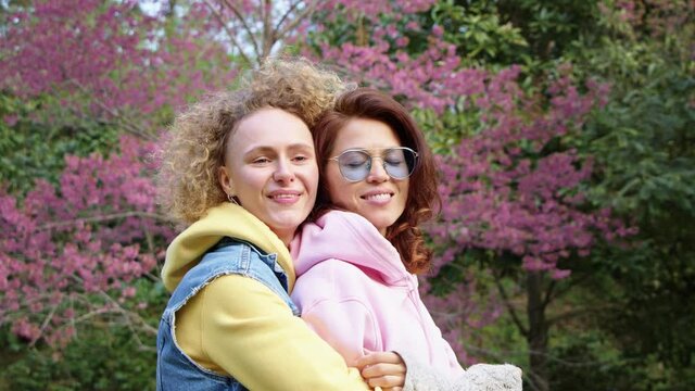 Homosexual lesbian couple hugging in a sakura garden and looks in to the camera. Two women share love and support. Gay Family. LGBT concept of friendship. cinematic chot bmpcc 6k