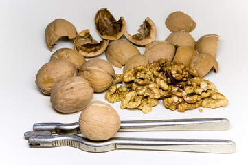 Walnuts are whole, the kernels of the nuts and their skins in the background. Hand-held nutcracker in the foreground.