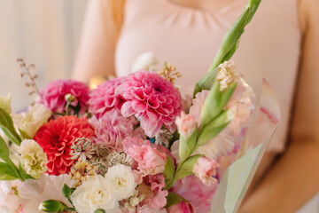 First dahlias, gladiolus, carnation, chrysanthemum and garden roses A young woman in a dress holds a beautiful bouquet in her hands on March 8 on a wooden background