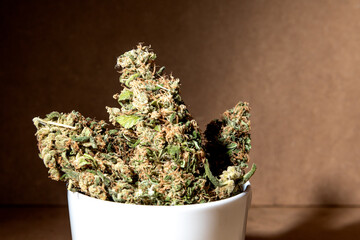 Details of medical marihuana buds inside a coffee cup. Selective focus on brown background.