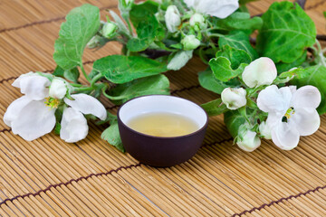Green tea in a ceramic cup with branches of blossoming apple tree on a bamboo background. Spring background.