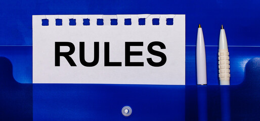 On a blue background, white pens and a sheet of paper with the text RULES