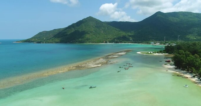 Thailand's ocean coast landscape aerial view: white sandy Malibu Beach and boats at water of Chaloklum Bay. Amazing Thai mountains island: forest, houses and resort. Rise up footage shot in 4K, UHD