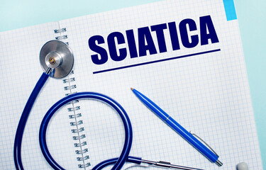 On a light blue background, an open notebook with the word SCIATICA, a blue pen and a stethoscope. View from above. Medical concept