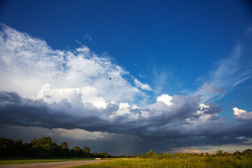 Small private plane climbs through the clouds. Aircraft is flying high above the beautiful landscape. Green field and runway in the sunset light after the thunderstorm