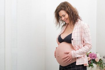Young beautiful pregnant woman standing near window at home  and touching sweetly her belly