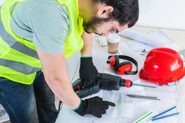 Fototapeta premium Architect, engineer with yellow safety vest, helmet and tools, working on some plans on desk.
