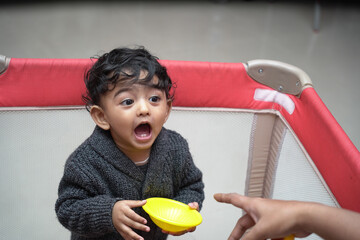 Adorable little Indian baby in a playpen screaming while holding a toy