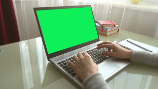 The girl working at home office hands on keyboard. The screen is a green background.
