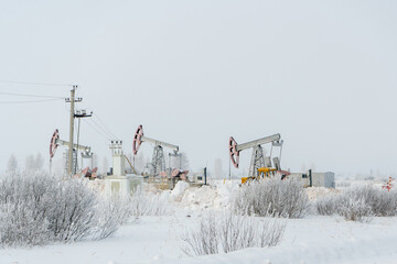 Oil rocking chair, winter landscape in Russia. A tractor clears snow from an oil production site