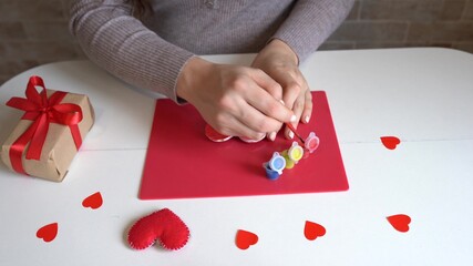 Valentine's day theme. Female hands paints red heart. gift, tools on white table. Workplace for the preparation of handmade ornaments