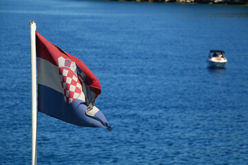 Flag of Croatia, blowing in the wind. Adriatic sea, island and boats in the background. Selective...