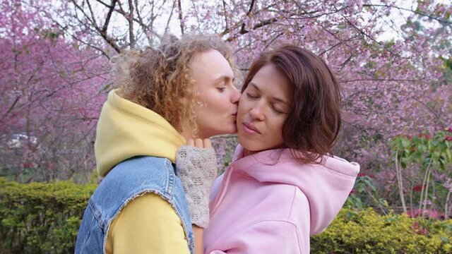 lesbian couple hugging in a sakura garden. Two women share love and support while holding hands. Gay Family. LGBT concept of friendship. cinematic chot bmpcc 6k