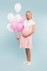 full length of pregnant woman holding balloons on blue