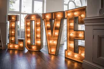 Wooden wedding love in capital letters with light up electric bulbs glowing bright orange stood on dance floor in marriage venue 