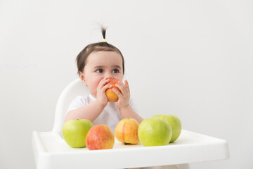 baby girl in baby chair eating apples and smiling on white background. Baby first solid food.