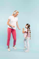 full length of happy mother and kid in wireless headphones dancing on blue