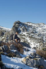 young mountaineer poses in the snow on the edge of a cliff with the mountains in the background in a very dangerous and impressive environment