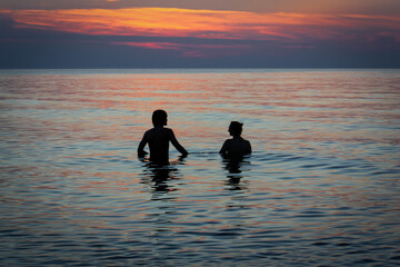 zakochana para chłopak i dziewczyna wchodzą do wody przy zachodzie słońca na plaży nad morzem bałtyckim - obrazy, fototapety, plakaty