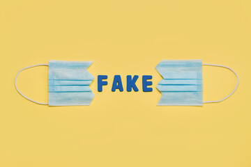 Protective surgical mask split in two with letters forming the word fake.Concept of protesting against coronavirus scams