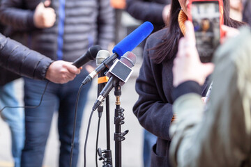 Microphones at press or news conference in the focus, mobile journalist filming media event with a...
