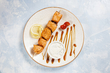 fish kebab with lemon and sauce on a white plate on a blue background top  view