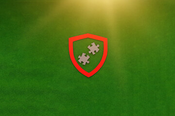 Knight's shield in red, two cardboard puzzles on a green background. The concept of protection, security.