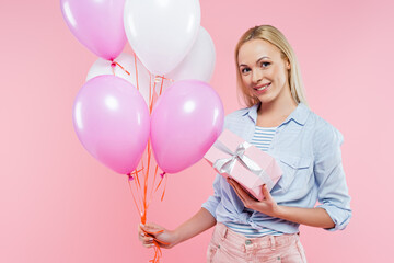 happy woman holding balloons and gift box isolated on pink