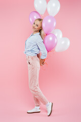 full length of cheerful woman standing and holding balloons on pink