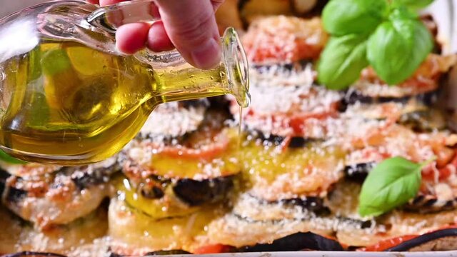 olive oil is poured into lasagna. Traditional italian food. Baked eggplant, tomatoes with sauce, parmesan and basil. Rustic food for a healthy diet. Vegetables for lunch.	