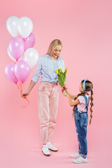 kid giving tulips to happy mother standing with balloons on pink