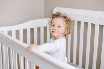 Cute adorable baby boy toddler standing in crib at kids nursery room at home. Funny charming baby...