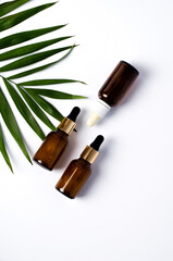 Serum in dark glass bottles, cosmetic oil on white background with palm leaf, flat lay, vertical image, copy space