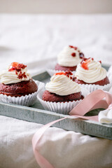 Homemade Red velvet cupcakes with whipped cream on wooden tray, white napkin with ribbon on white linen table cloth.