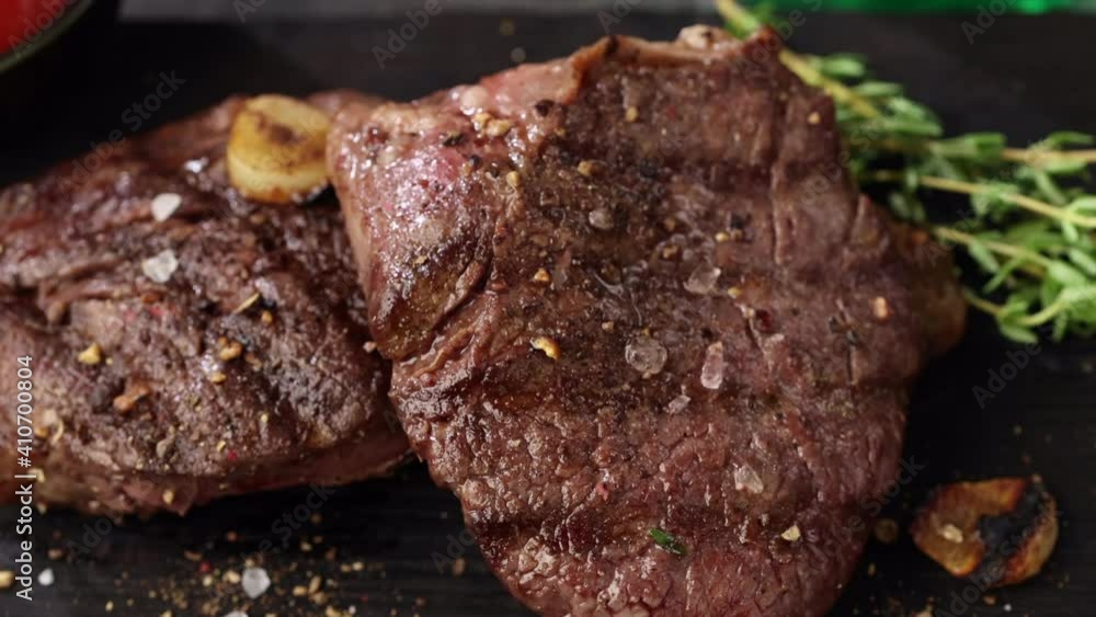 Poster close up of freshly grilled beef steak meat with spices on black stone plate, top view zoom in