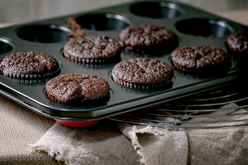 Fresh baked homemade chocolate cupcakes muffins in form for cooking standing on kitchen table with...