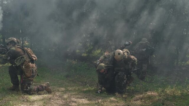 Handheld footage of soldiers dragging their wounded friend along smoky battlefield, saving him by applying tourniquet to his leg