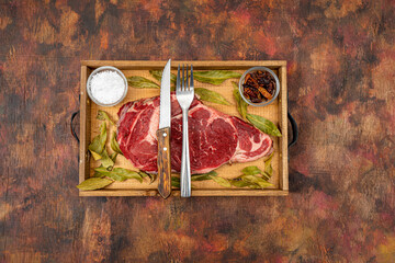 Raw beef ribeye on a round slate plate with glass containers containing peppercorns, coarse salt...